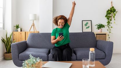 A woman sitting on her sofa makes a celebratory gesture.