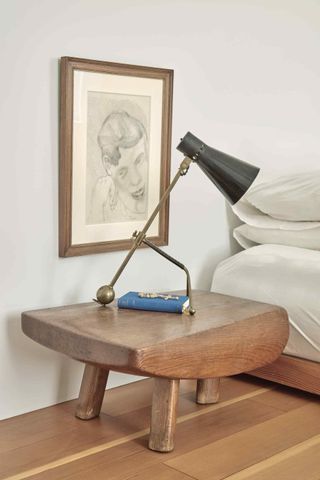 A chunky wooden low table and lamp, pencil portrait of a man framed on the wall