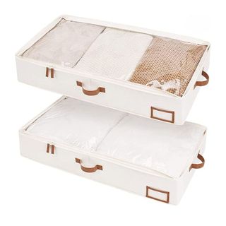 A pair of cream fabric underbed storage containers full of sweaters, with brown leather look handles and detailing