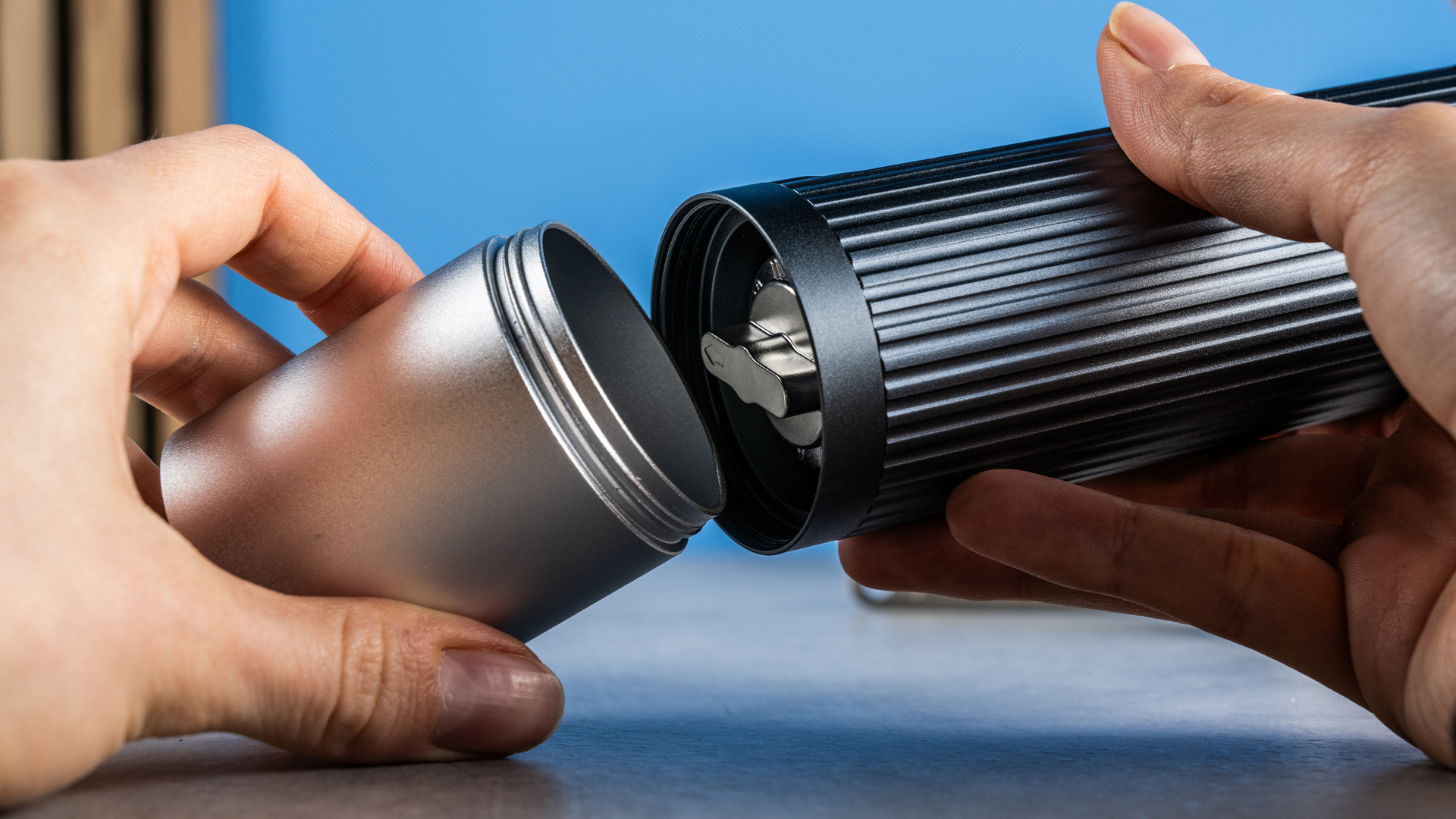 the aeropress manual coffee grinder in gray and silver against the tom's guide blue background