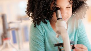 best microscope - young girl looking into microscope with one eye closed