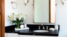Narrow bathroom ideas can be sleek and stylish. Here is a white bathroom with a white and black sink and wooden door frame