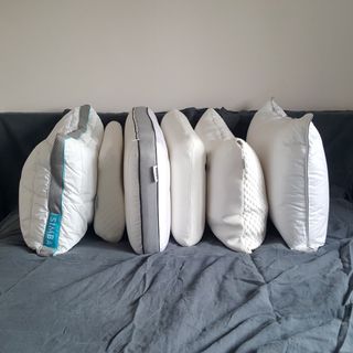 A group of pillows of different shapes and sizes on a bed with grey linen bedding