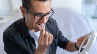 A man looks in the mirror while placing a transparent dental guard into his mouth