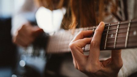 Closeup of woman playing a barre chord on an electric guitar.