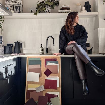 Natalie Jahangiry sat on her kitchen work tops with a board of colour swatches to consider