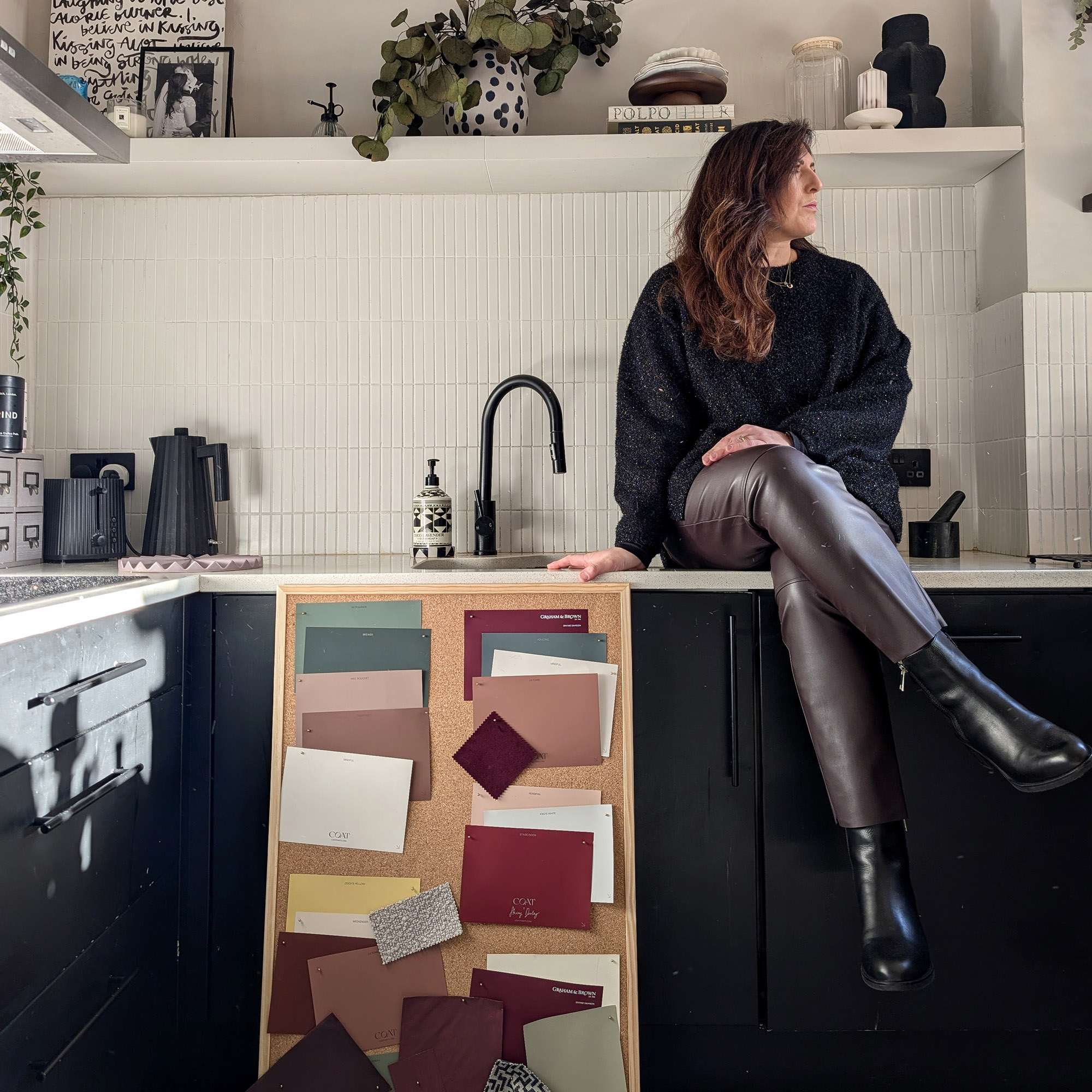 Natalie Jahangiry sat on her kitchen work tops with a board of colour swatches to consider