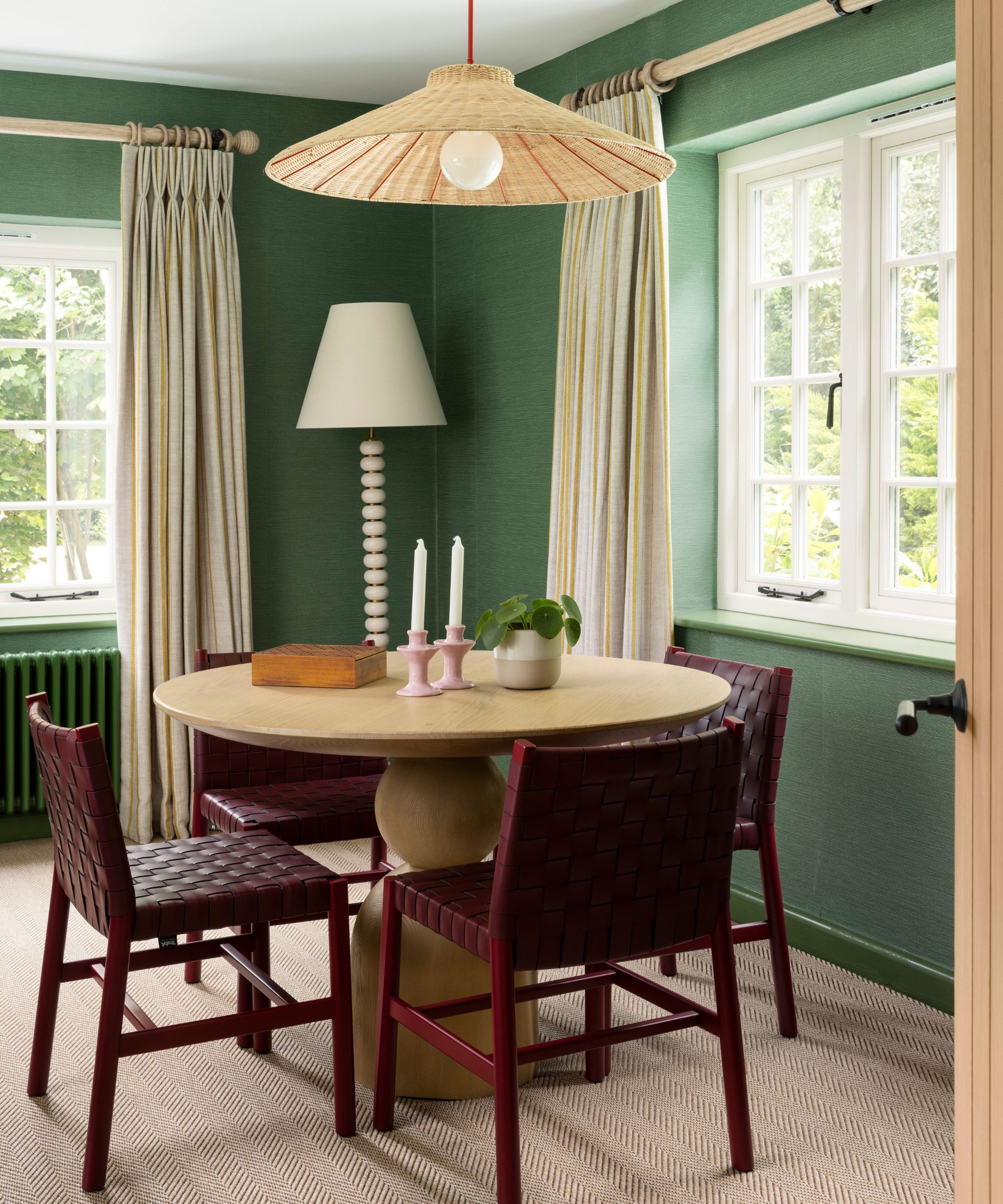 an emerald green drawing room with a small dining table set up with burgundy woven chairs and a round wooden pedestal table