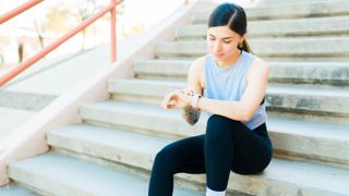 Woman sitting on stairs checking sports watch