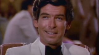 Pierce Brosnan smiles while sitting in a tuxedo in Remington Steele.