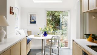 small kitchen diner area with white table and build in seating at end of kitchen next to glazed panel