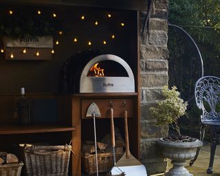 A stainless steel pizza oven in a bricked patio seating area with twinkling fairy lights