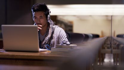 Young man studies his laptop in an otherwise empty classroom.