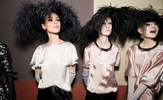 Three models wearing light clothes featuring feathers and a headpiece