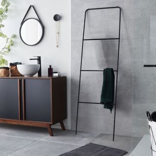 Ebern Designs Brecker Free Standing Towel Rack in black standing in grey tiled bathroom