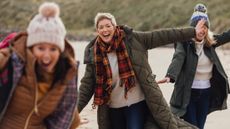 A medium close up of a group of mature women who are twirling on the beach and having fun whilst out together on a walk. 