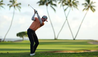 Alex Smalley strikes an iron shot from the rough in front of palm trees which are in the shape of a W