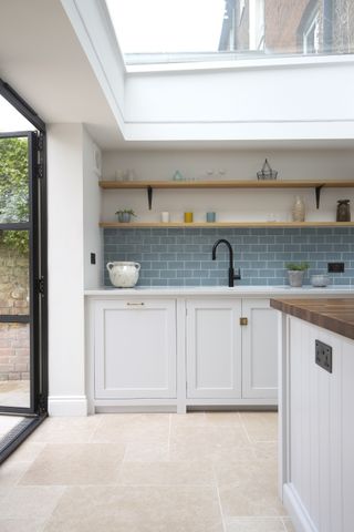 white kitchen with stone flooring, crittal doors, island, blue splash back and open shelving