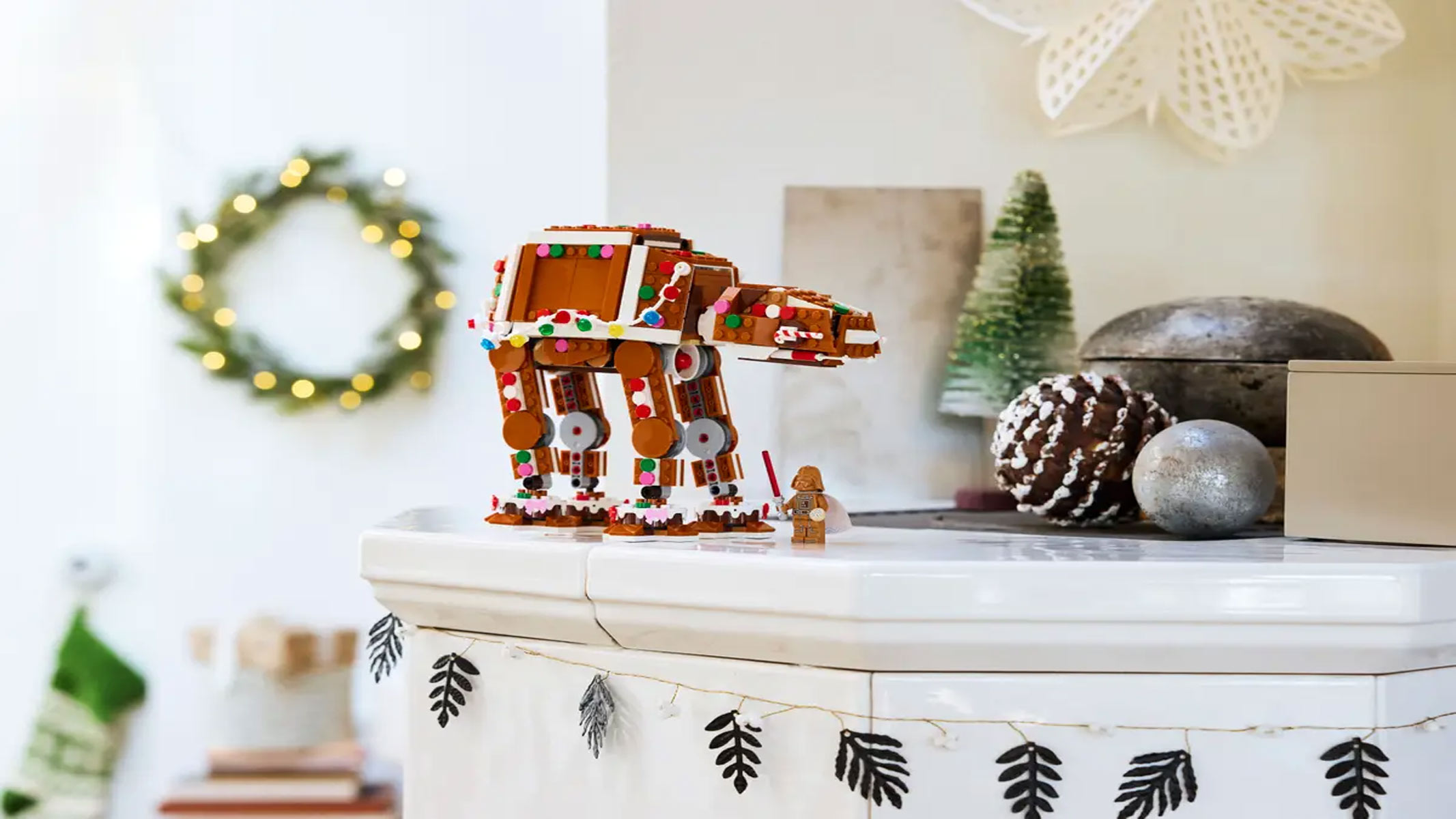A Gingerbread-colored camel-like robot is displayed on a white surface with with a wreath and a small Christmas tree in the background.