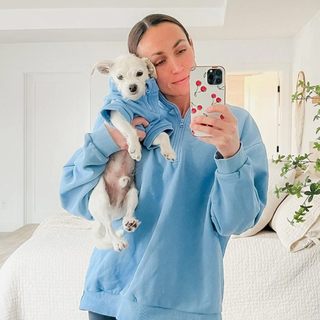 Woman taking a selfie in the mirror, holding her dog and wearing a matching blue quarter zip sweatshirt