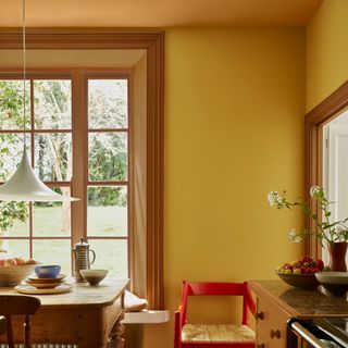 A yellow-painted kitchen with a slightly darker ceiling and a contrasting red chair