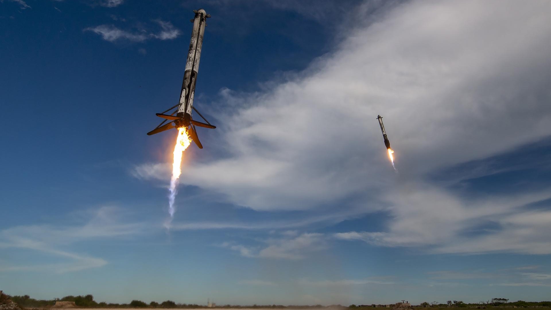 two white rockets make their way to the ground, each with four landing legs extended as their engines expel small plumes of fire