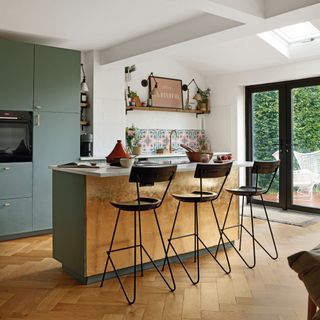 wooden kitchen island, wooden flooring, and dark green cabinets in open plan kitchen