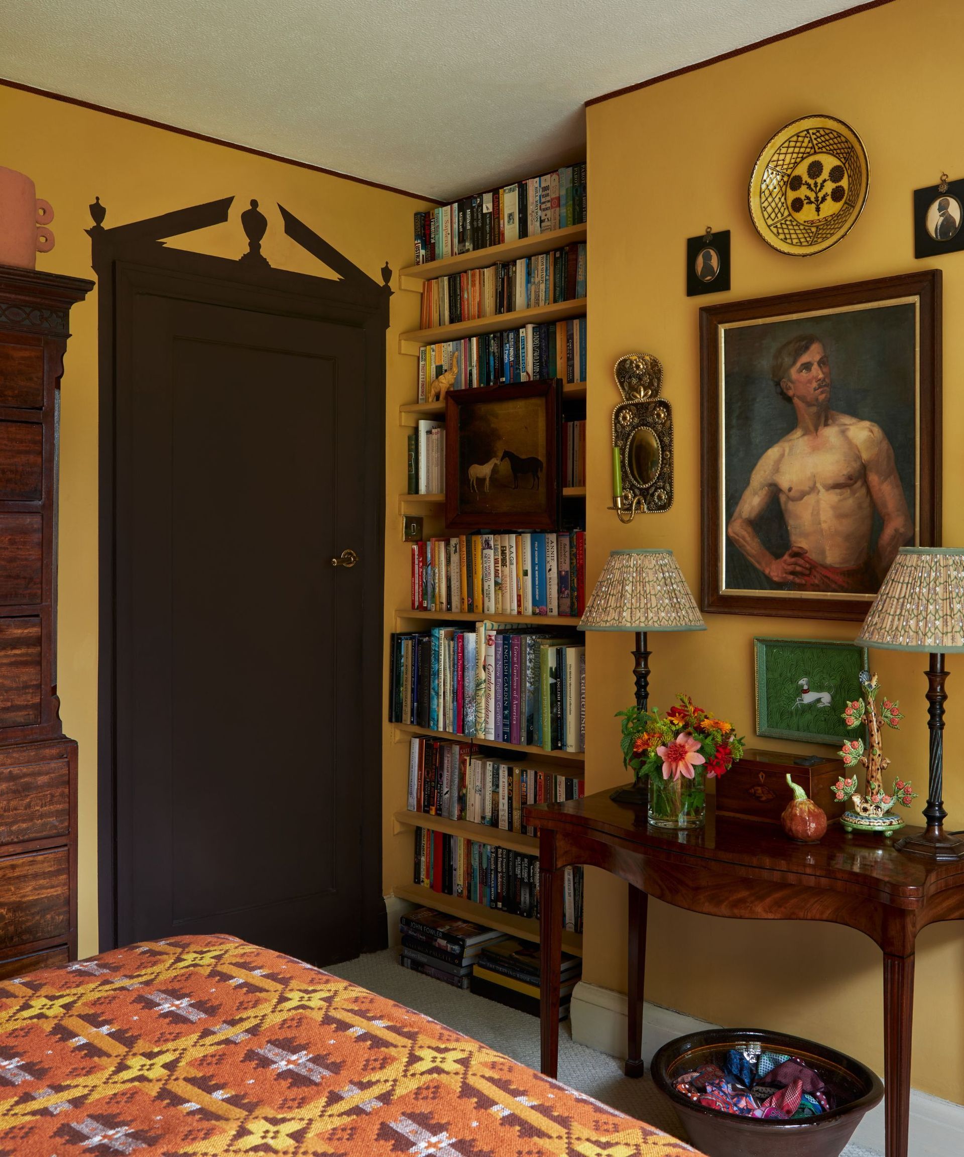 A colorful bedroom with walls painted in yellow, adorned with paintings and accessories. The bedroom door is painted in deep brown color with a decorative painted design at the top of the door.
