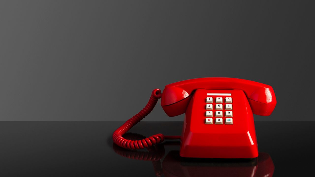 A red telephone sits on a desk.