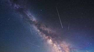 meteor shower trails appear as long white streaks of light against a milky way backdrop.