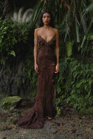 A bias-cut Mirror Palais brown gown worn by a model on the beach in front of trees