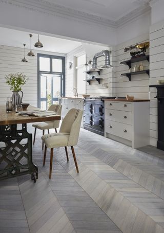 A kitchen in a modern rustic style with white appliances and light grey wooden chevron flooring