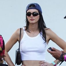 Kendall Jenner wearing a white tank top, baseball cap, and white cut-off denim shorts with black boots at Coachella weekend one, 2026