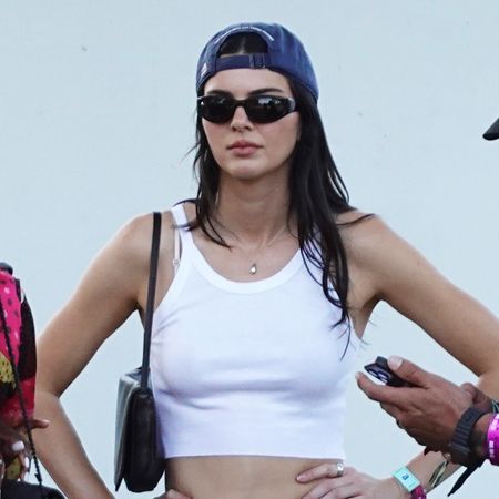 Kendall Jenner wearing a white tank top, baseball cap, and white cut-off denim shorts with black boots at Coachella weekend one, 2026