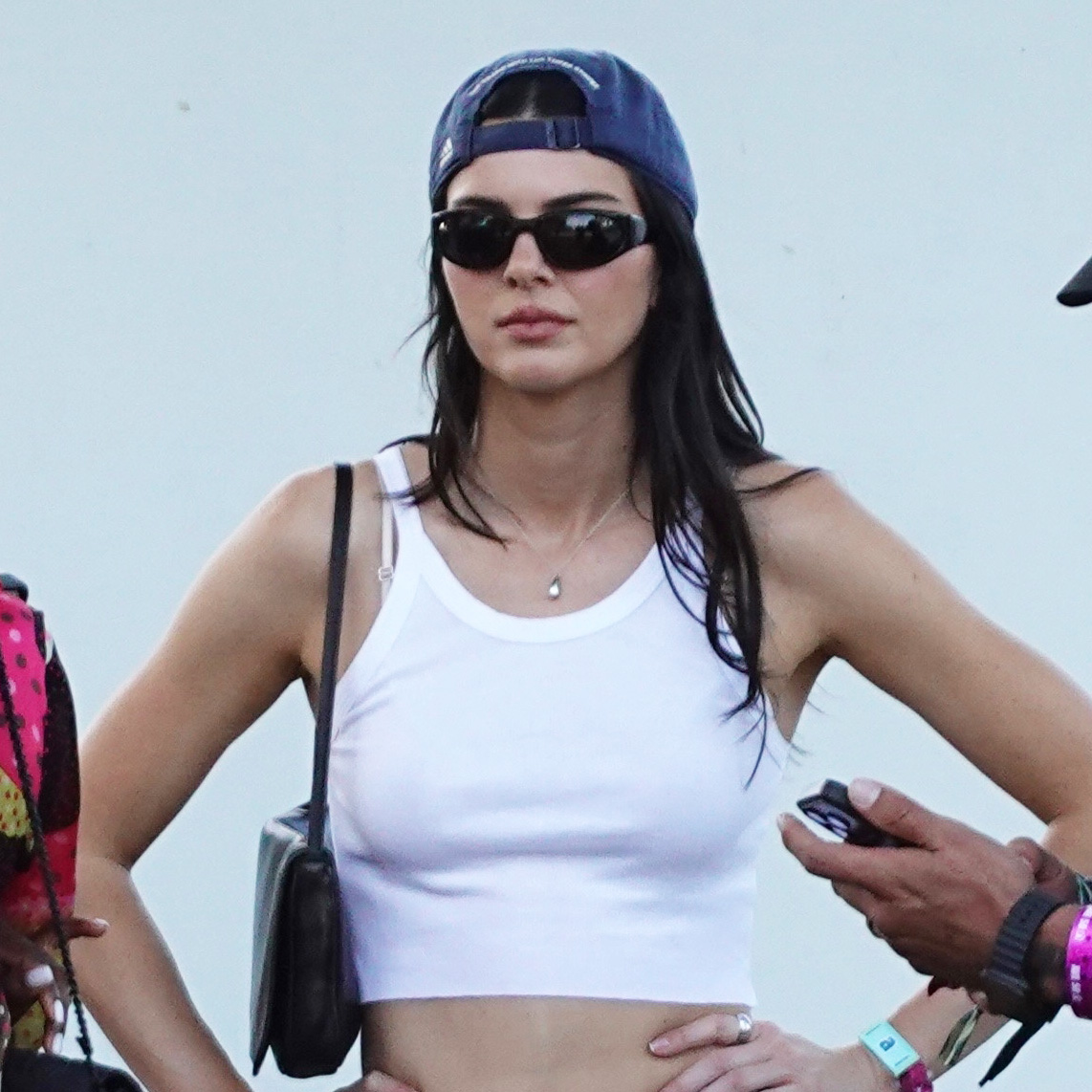 Kendall Jenner wearing a white tank top, baseball cap, and white cut-off denim shorts with black boots at Coachella weekend one, 2026