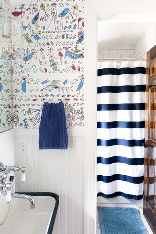 kids bathroom with hand colored wallpaper, blue and white stripe shower curtain, blue towel and rug, shiplap walls, enamel sink