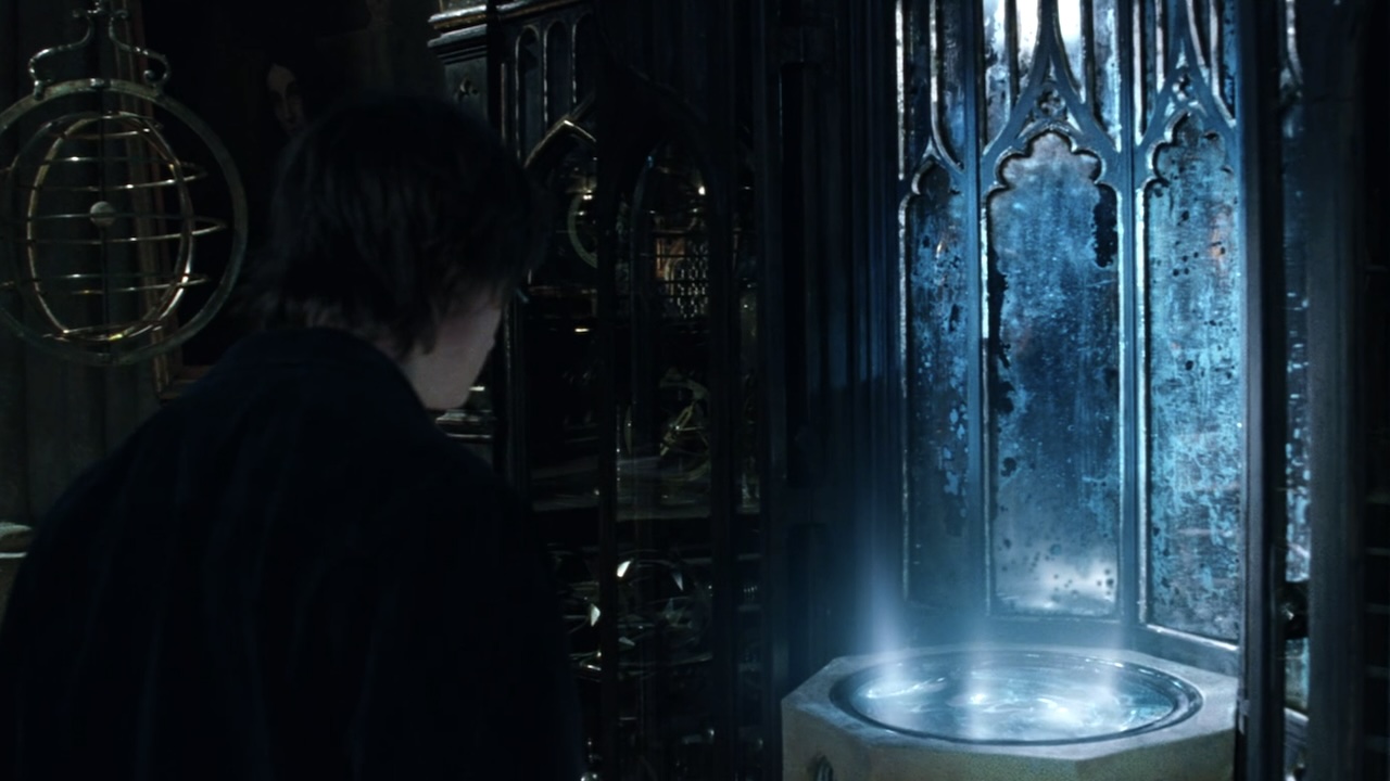 Harry looking at a pensieve that's glowing blue light.