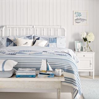 bedroom with white striped wall white floor and white bed with blue designed cushions