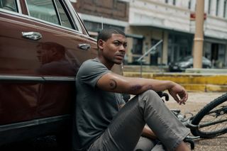 Aaron Pierre as Terry Richmond, sitting with his back against a car and a fallen bicycle next to him, in Rebel Ridge.