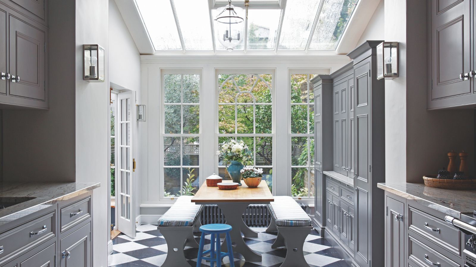 Gray kitchen cabinets and checkerboard tiles floor, conservatory room with wood dining table and benches