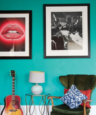 Funky gallery wall featuring neon lips design and mono print, on aqua wall, with green velvet chair, guitar, and metal side table with lamp.