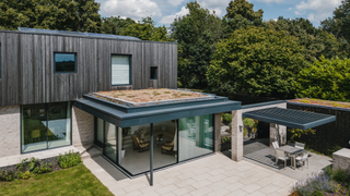 Exterior view of a cladded house with a pergola on the patio in the garden and solar panels on the roof