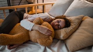 A woman sleeps soubdly while hugging a giant teddy bear