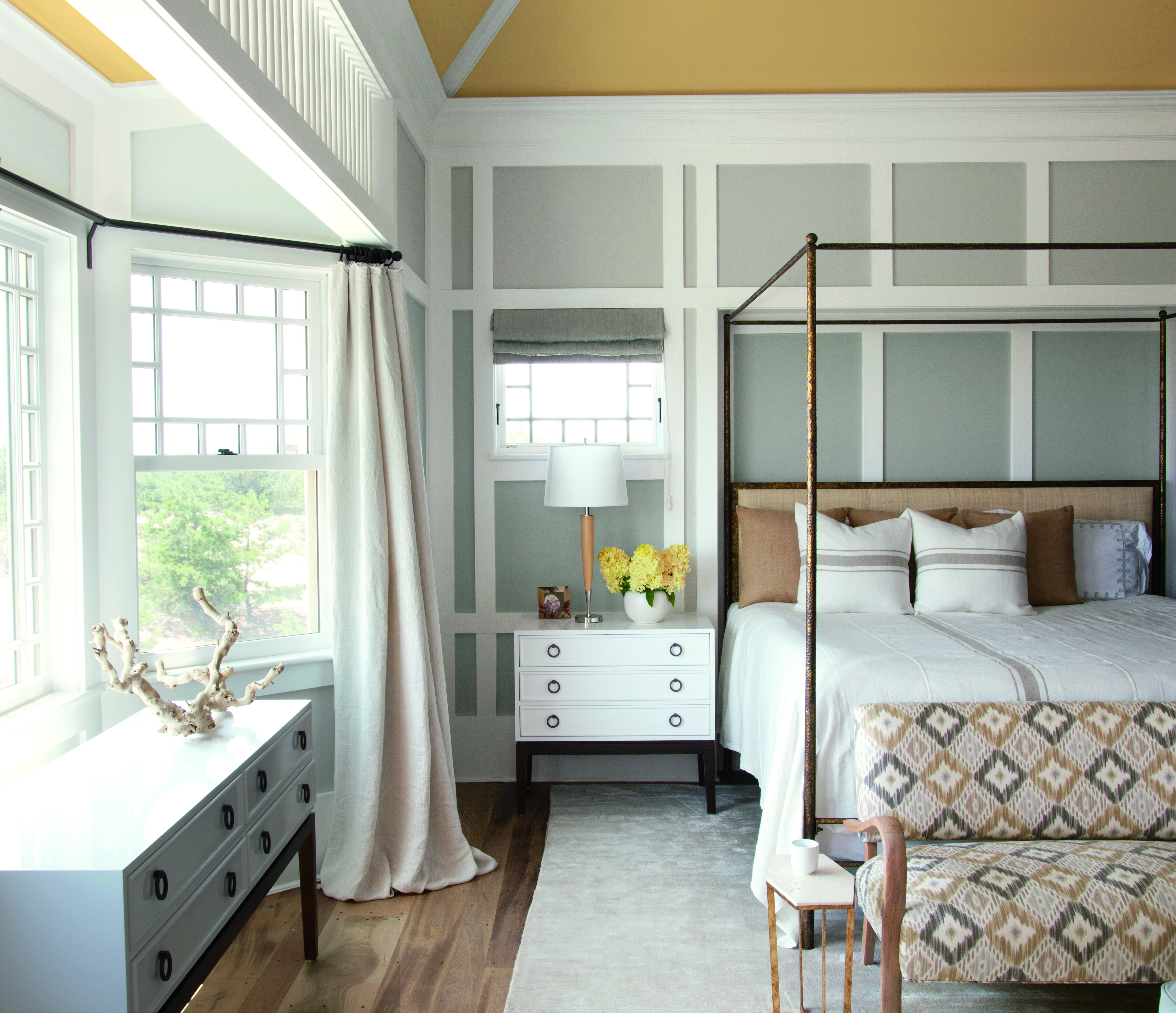 The best bedroom colors illustrated in a pale blue-gray and white scheme with wall panelling, white furniture and a bronze four poster bed with white bed linen.