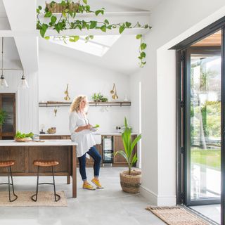 woman stood in open plan kitchen with glass bi fold doors opening to garden