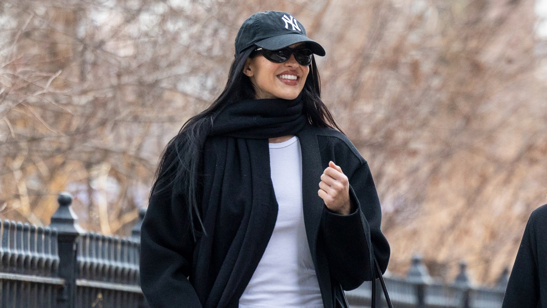 Amelia Gray wearing a Yankees baseball cap, black scarf and coat, white T-shirt, baggy jeans, and black glove flats