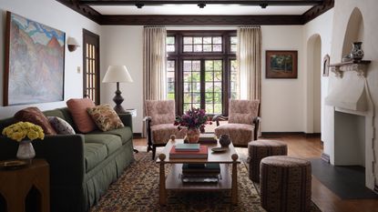 A wide view of a living space showing a green sofa, a landscape painting, and an ornate white plaster fireplace with a pointed arch alcove