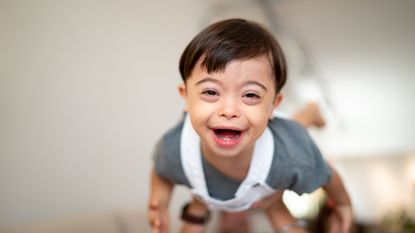 A mom tosses her smiling toddler in the air. He has Down Syndrome.