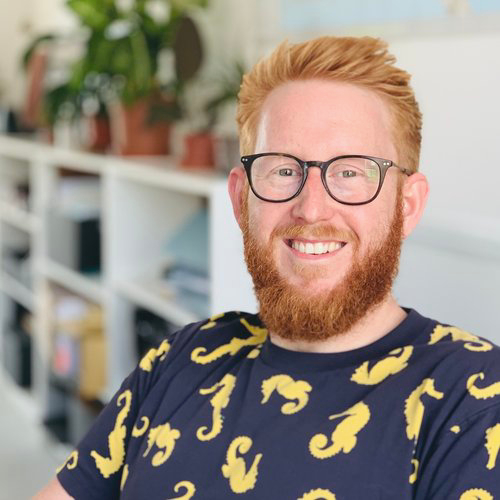 male with red hair and beard wearing glasses and blue tshirt with yellow seahorse pattern