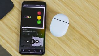 Poweramp Music Player app on an Android phone kept on a wooden table next to some white TWS earbuds.